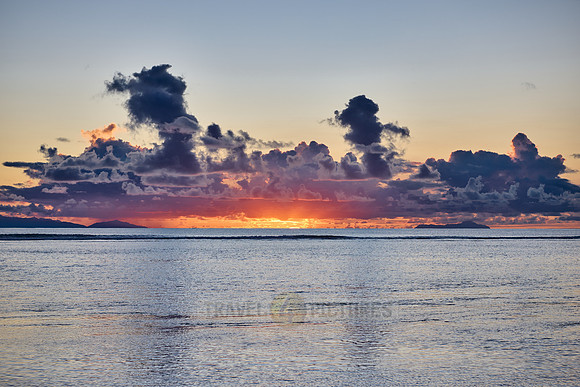 Sunset with palm leafes and clouds over the sea from the Anse Source D'Argent