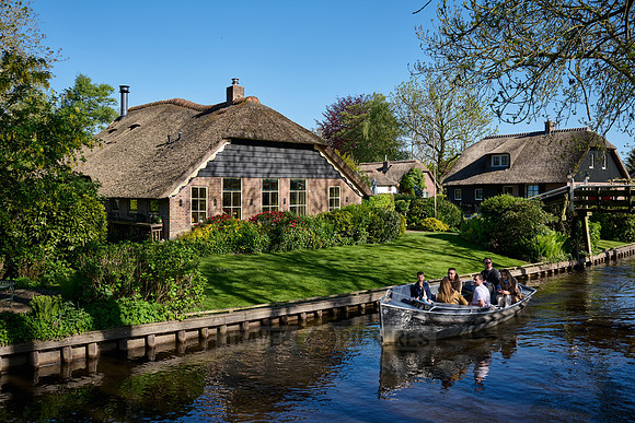 tourists in boat on canal and traditional house in dutch Giethoorn village