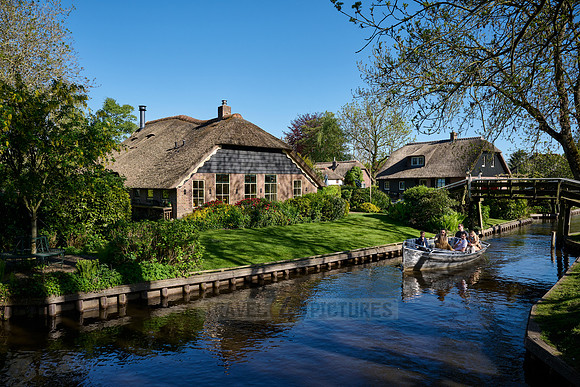 tourists in boat on canal and traditional house in dutch Giethoorn village