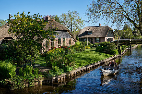 tourists in boat on canal and traditional house in dutch Giethoorn village