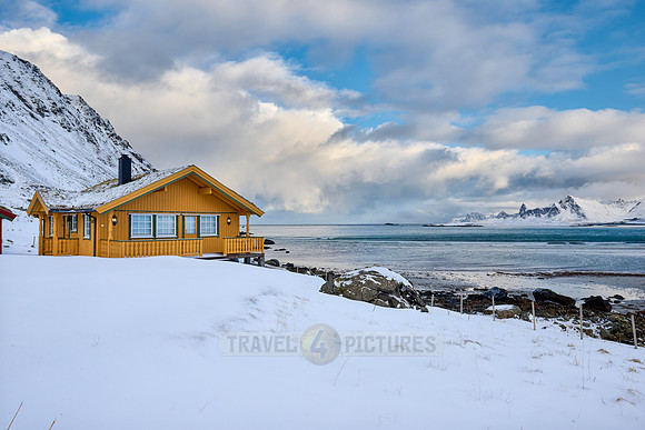 yellow house in winter landscape with sea and mountains at Sandbotnen, Lofoten