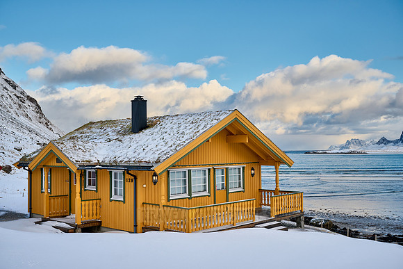 yellow house in winter landscape with sea and mountains at Sandbotnen, Lofoten