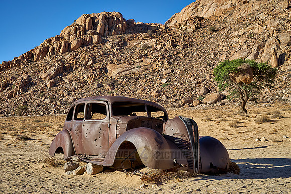 rusty old car with bullet holes in desert landscape