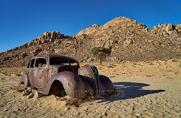 rusty old car with bullet holes in desert landscape