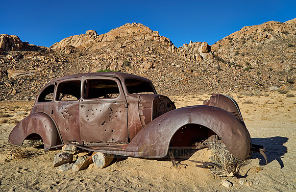 rusty old car with bullet holes in desert landscape
