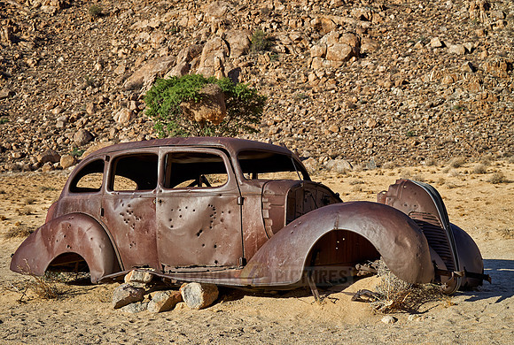 rusty old car with bullet holes in desert landscape
