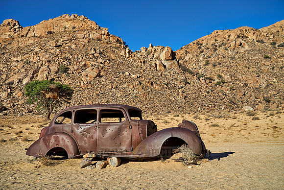 rusty old car with bullet holes in desert landscape