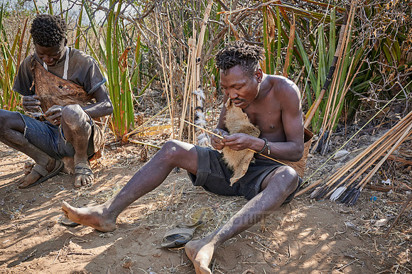 bushmen of Hasabe tribe sitting around a fireplace and carving an arrow
