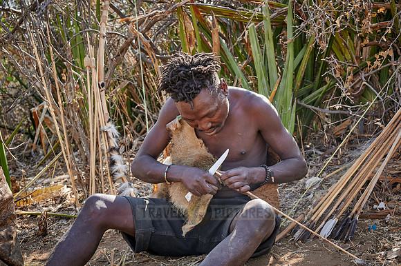 bushmen of Hasabe tribe sitting around a fireplace and carving an arrow