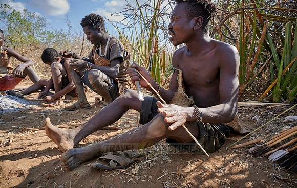 bushmen of Hasabe tribe sitting around a fireplace and carving an arrow