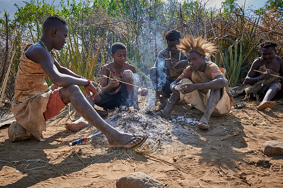 bushmen of Hasabe tribe sitting around a fireplace and broiling a bird