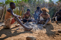 bushmen of Hasabe tribe sitting around a fireplace and broiling a bird