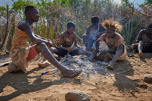 bushmen of Hasabe tribe sitting around a fireplace and broiling a bird