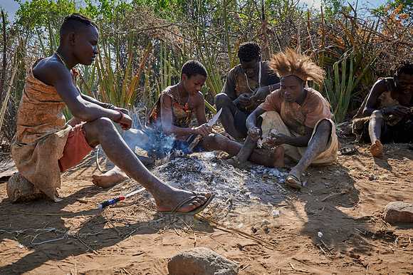 bushmen of Hasabe tribe sitting around a fireplace and broiling a bird