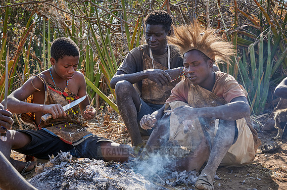 bushmen of Hasabe tribe sitting around a fireplace and broiling a bird