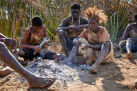 bushmen of Hasabe tribe sitting around a fireplace and broiling a bird