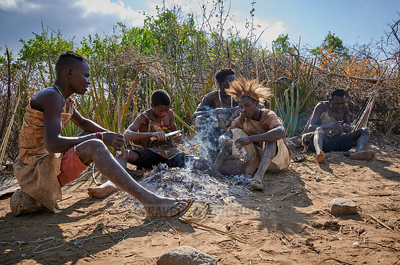 bushmen of Hasabe tribe sitting around a fireplace and broiling a bird