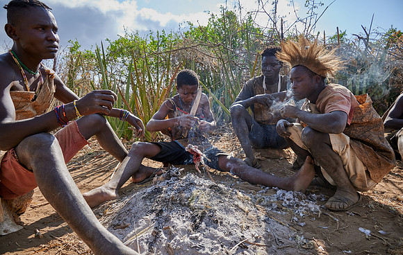 bushmen of Hasabe tribe sitting around a fireplace and broiling a bird