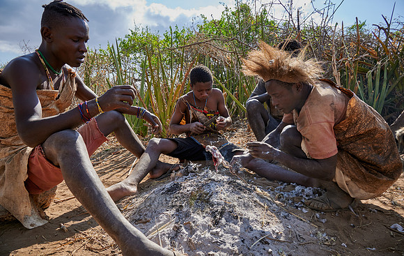 bushmen of Hasabe tribe sitting around a fireplace and broiling a bird