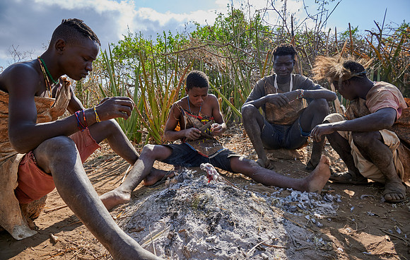 bushmen of Hasabe tribe sitting around a fireplace and broiling a bird