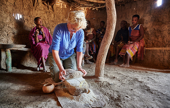 tourist grind flour on a stone with group of women of Datoga tribe
