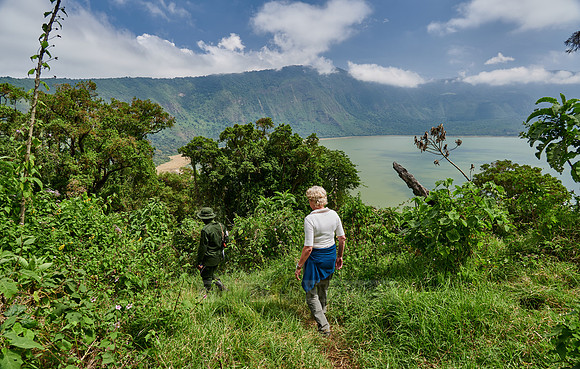 Tourist and Ranger walking through forest down to Lake Empakaai