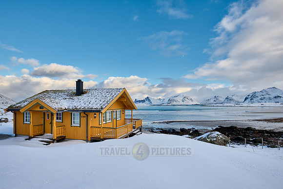 yellow house in winter landscape with sea and mountains at Sandbotnen, Lofoten
