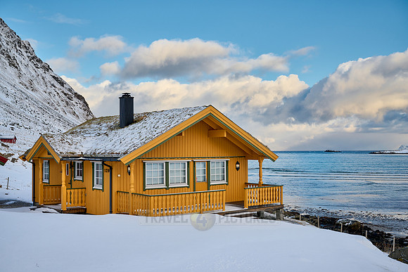 yellow house in winter landscape with sea and mountains at Sandbotnen, Lofoten