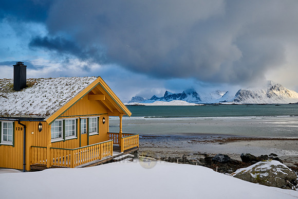 yellow house in winter landscape with sea and mountains at Sandbotnen, Lofoten