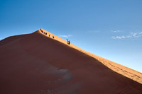 group of people climbing up sand dune of Namib desert