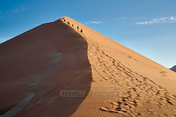 group of people climbing up sand dune of Namib desert