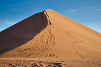 group of people climbing up sand dune of Namib desert