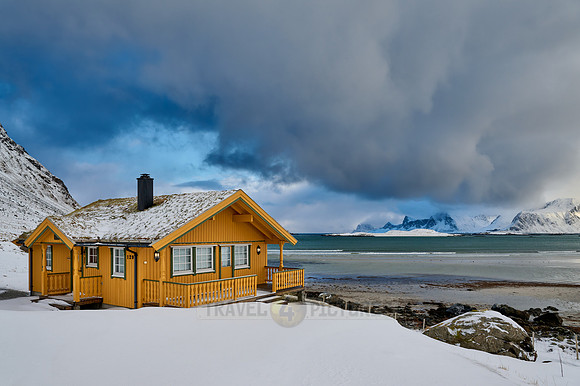 yellow house in winter landscape with sea and mountains at Sandbotnen, Lofoten
