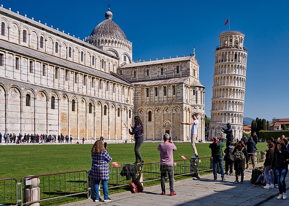 Tourists try to symbolically hold on to the Leaning Tower of Pisa