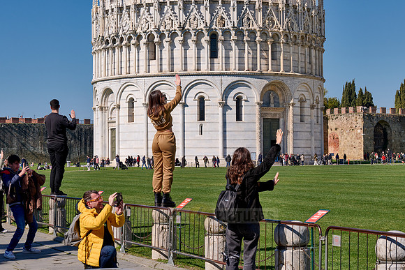 Tourists try to symbolically hold on to the Leaning Tower of Pisa