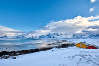 yellow house in winter landscape with sea and mountains at Sandbotnen, Lofoten