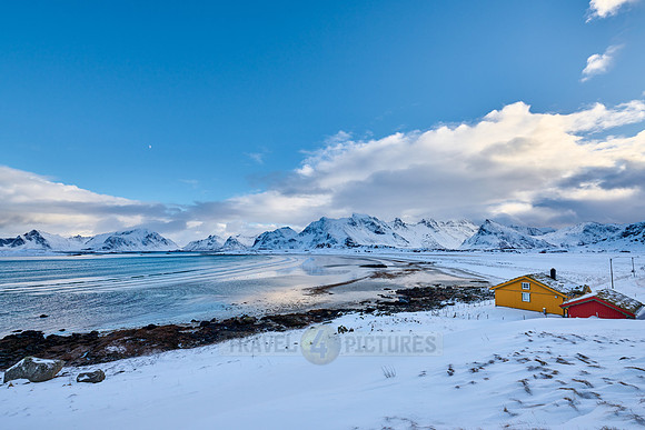 yellow house in winter landscape with sea and mountains at Sandbotnen, Lofoten