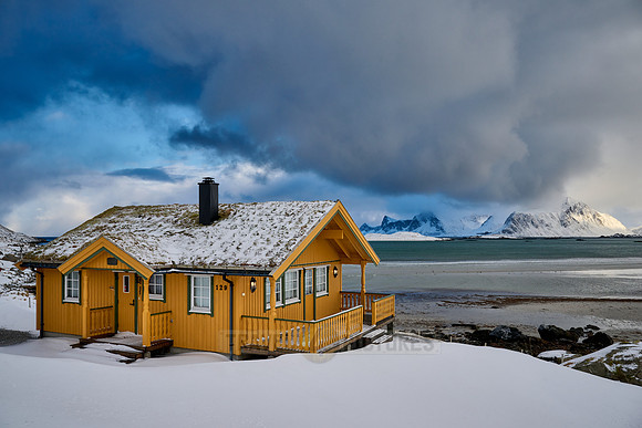 yellow house in winter landscape with sea and mountains at Sandbotnen, Lofoten