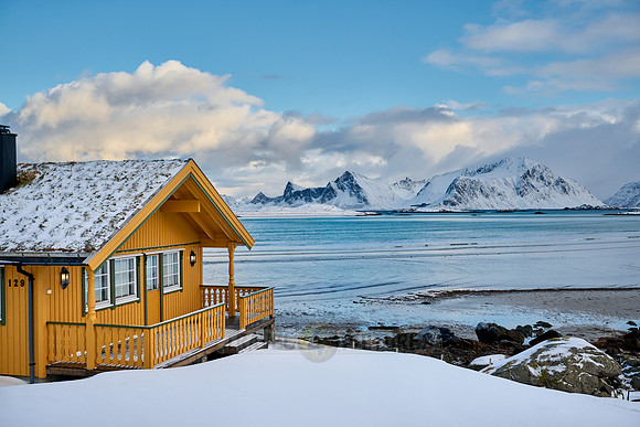yellow house in winter landscape with sea and mountains at Sandbotnen, Lofoten