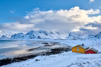 yellow house in winter landscape with sea and mountains at Sandbotnen, Lofoten