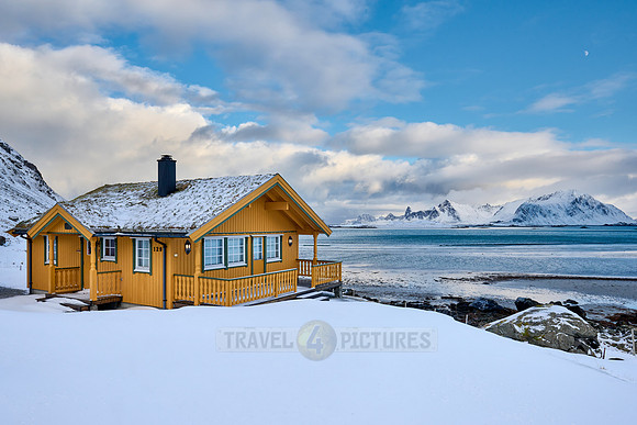yellow house in winter landscape with sea and mountains at Sandbotnen, Lofoten