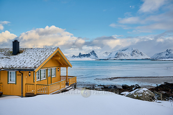 yellow house in winter landscape with sea and mountains at Sandbotnen, Lofoten