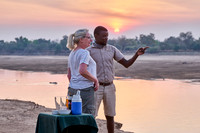 Tourist und Guide beim Sundowner am Luangwa-Fluss. |tourist and guide taking sundowner at Luangwa river|